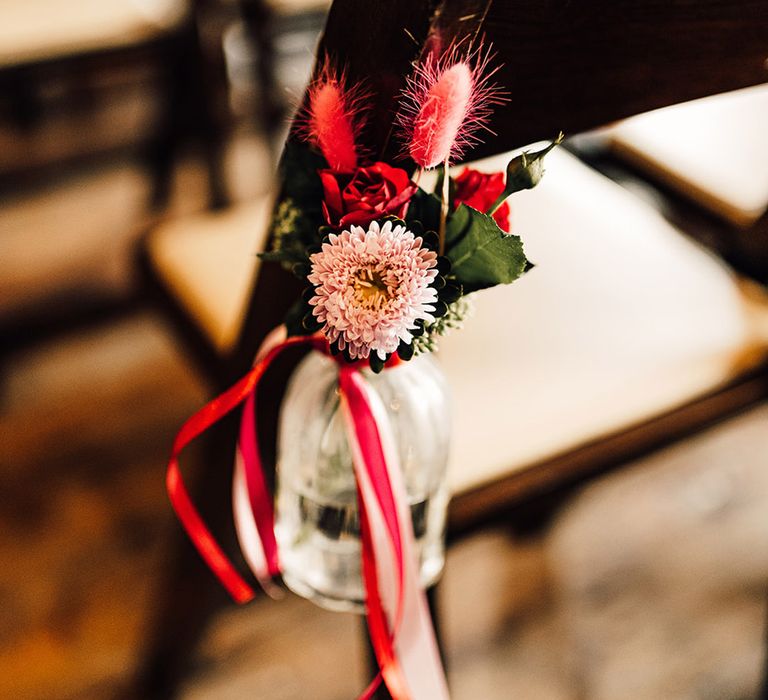 pink chair back wedding flowers in a bottle tied with ribbon 