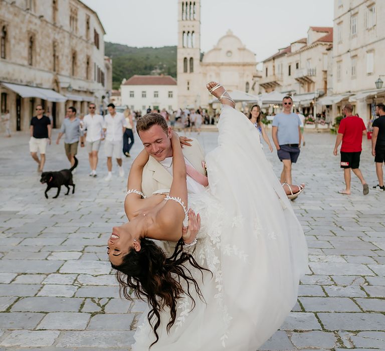 Groom in linen suit dips bride in 3D lace wedidng dress in the middle of Hvar Old Town In Croatia