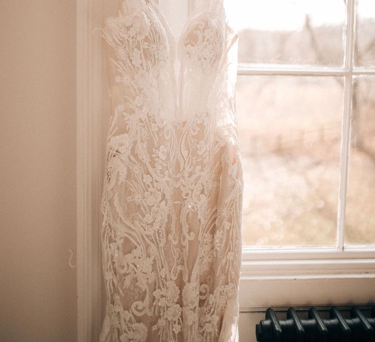 Lace embellished wedding dress hanging on white coat hanger at Aswarby Rectory 