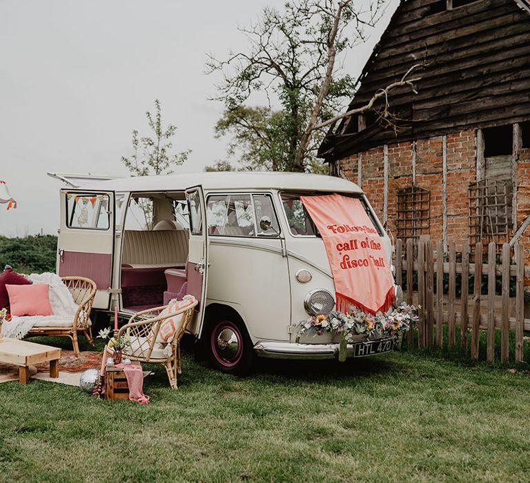 Red and pink retro wedding banner sign on top of vintage campervan transport with cosy seating area 