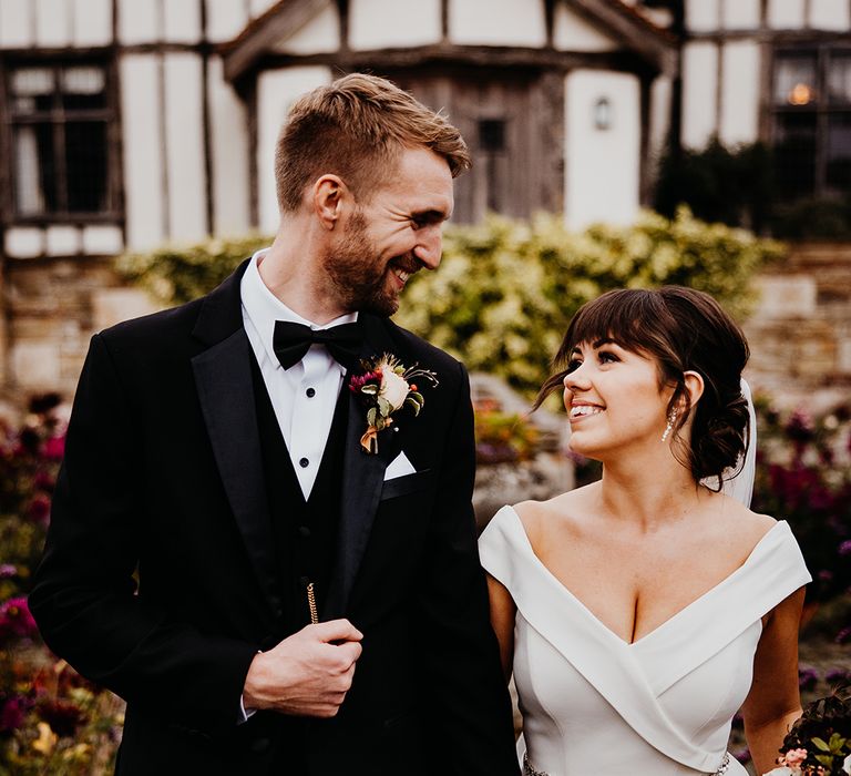 Groom in black tuxedo walking with the bride in a bespoke off the shoulder wedding dress