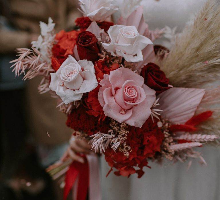 London wedding with the bride holding a pink and red wedding bouquet of roses with dried dyed palm leaves and pampas grass 