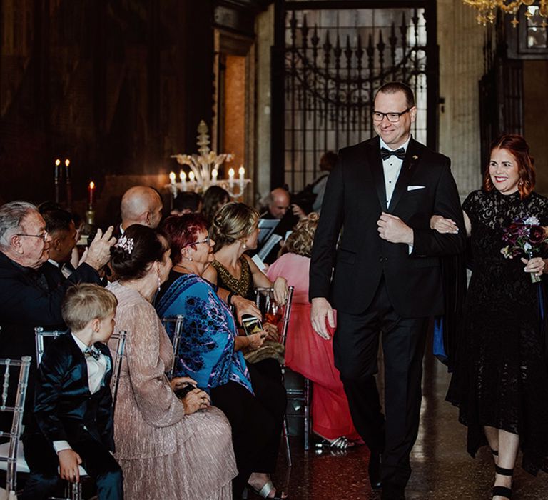 Bridesmaid in black bridesmaid dress walking with groomsman down the aisle 