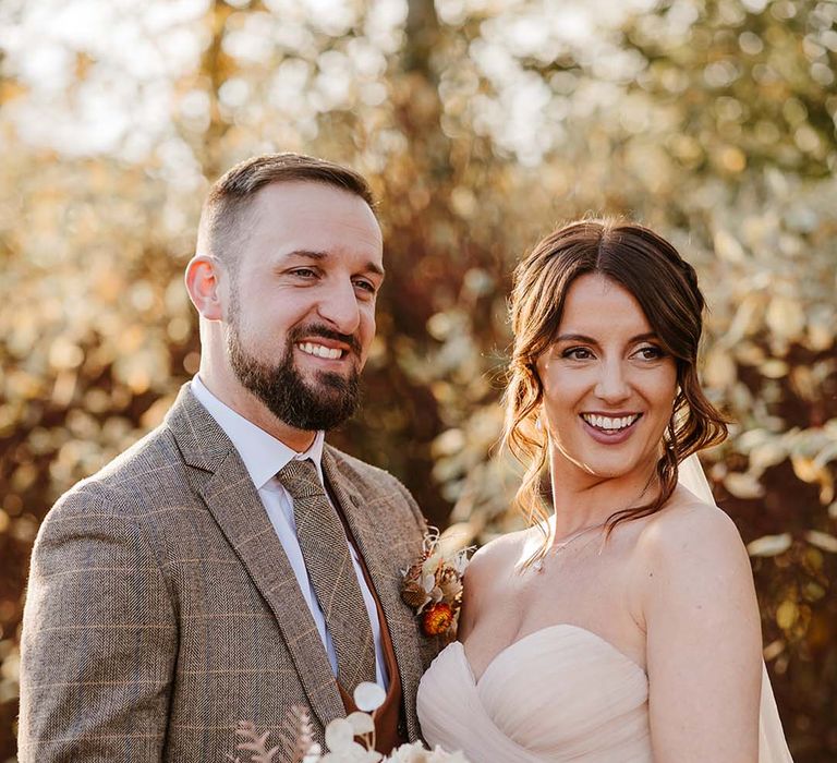 Groom in three piece brown wedding suit with bride in strapless ruffle wedding dress holding boho bouquet for autumnal wedding 