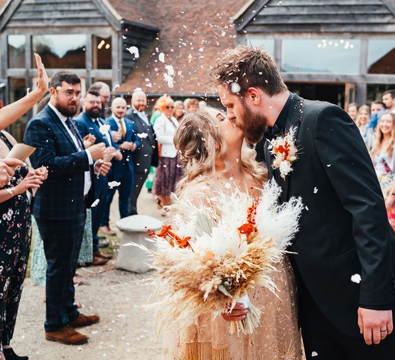 Bride in gold wedding dres with pampas grass wedding bouquet kissing groom for their confetti moment 