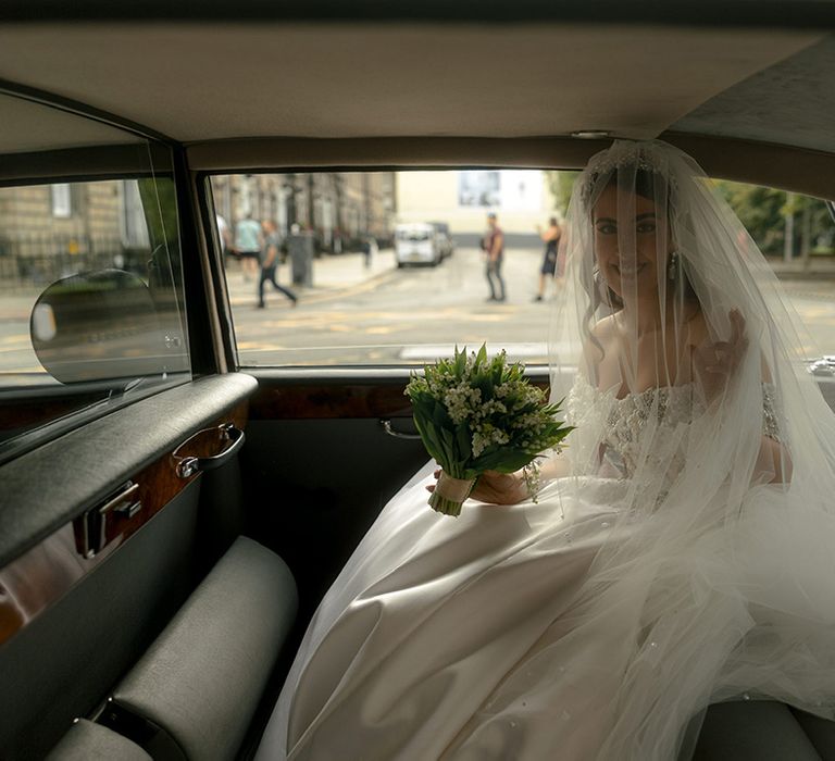 Bride sitting in the back of the wedding car on the way to the wedding venue 