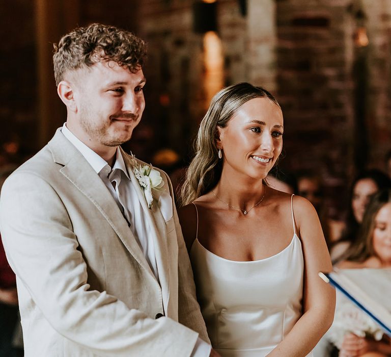 Bride in slip wedding dress and groom in beige suit stand side by side at the wedding ceremony 