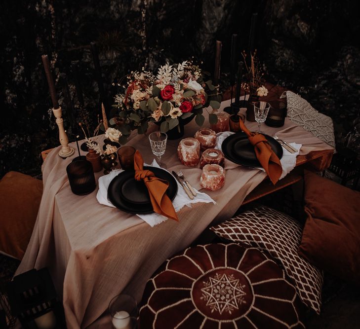 Autumnal wedding table setting for two with black plates and orange ribbons with black candles and a centrepiece with roses