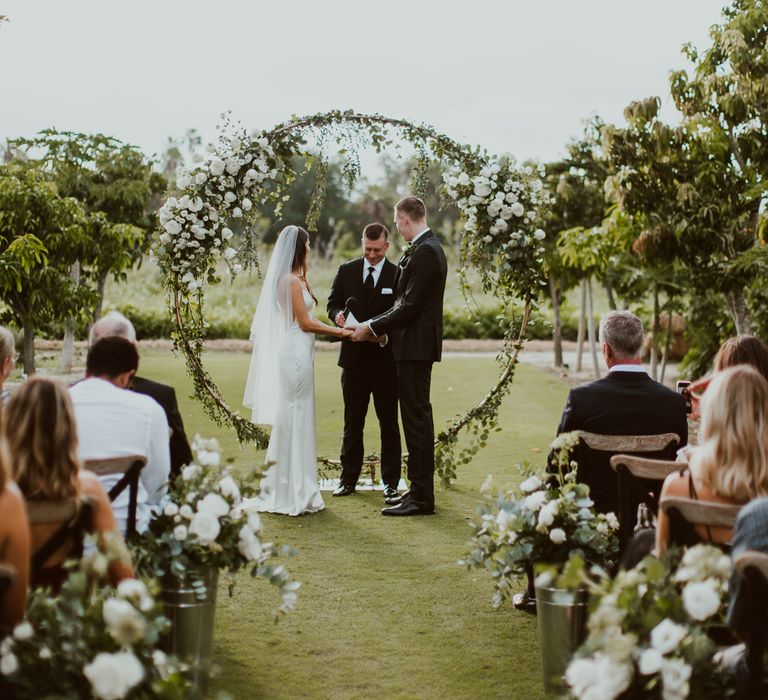 Bride and groom get married in front of a white flower arch