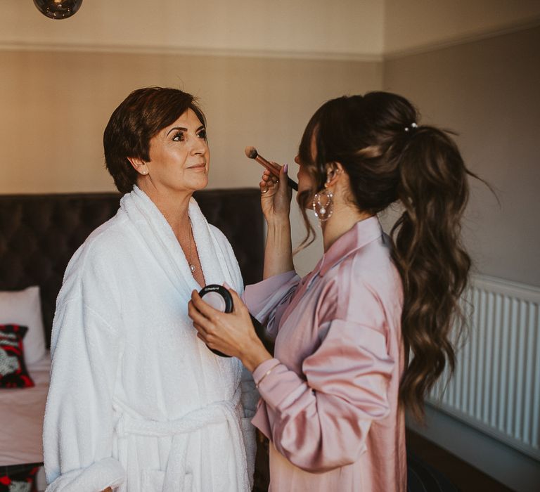 Mother of the bride has makeup done on bride's wedding morning