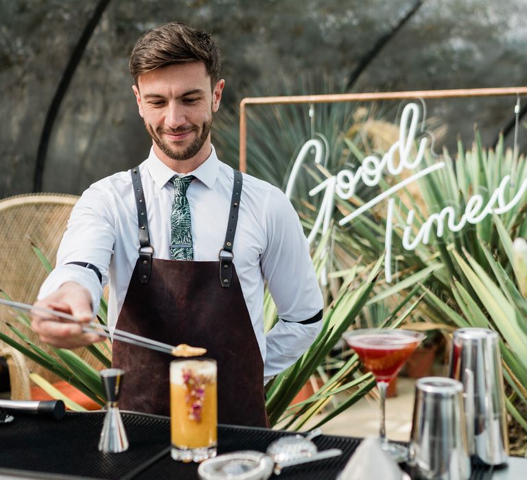 Man behind bar garnishes orange cocktail in front of 'Good Times' Neon Sign at Urban Jungle Suffolk