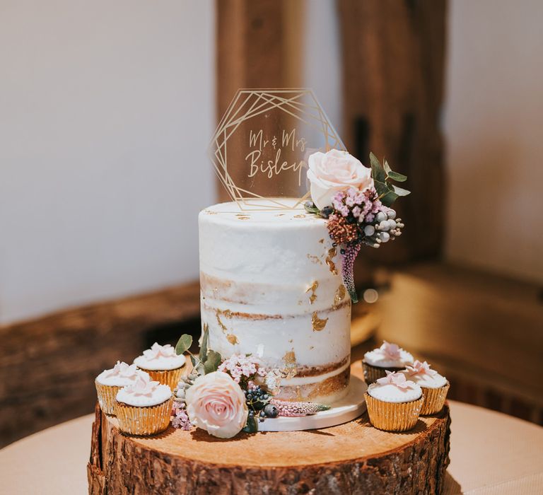 Naked cake upon tree trunk surrounded by cupcakes