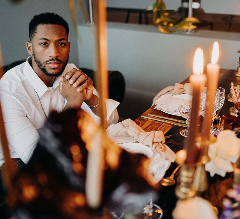 Black bearded groom sitting at an intimate table in a white shirt 