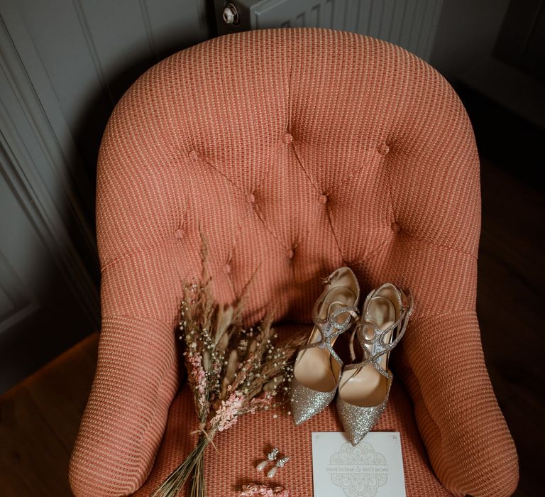 Orange chair with sparkly Jimmy Choo bridal shoes, pear drop earrings and dried flower wedding bouquet 