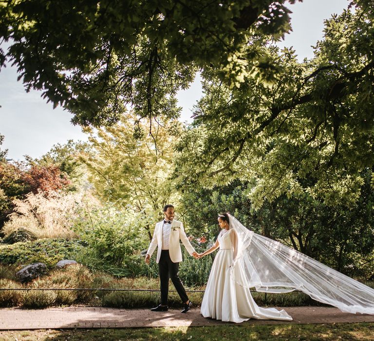 Ethiopian wedding with groom in a white tuxedo jacket leading his princess bride in a full skirt dress and long veil 