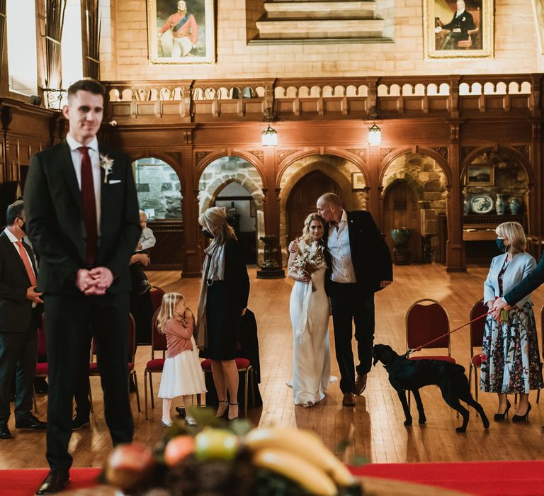 Bride walks down the aisle with her father on the day of her wedding as he kisses her head