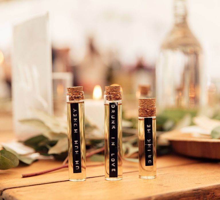 Three thin glass corked tequila wedding favours with typewritten labels on wooden table