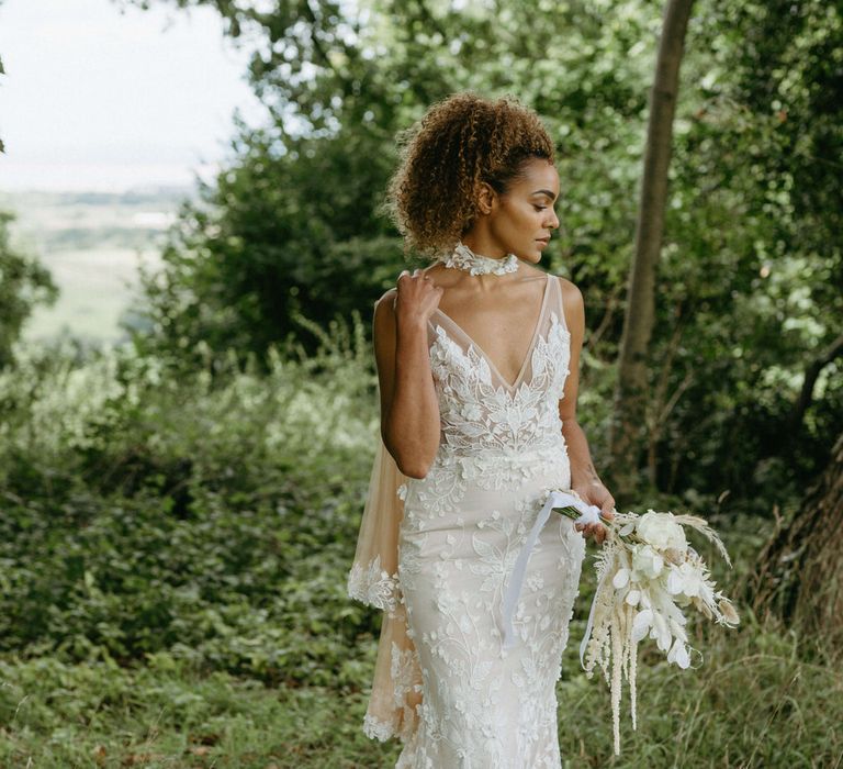 Boho bride in the woods at Berwick Lodge wearing floral lace embroidered wedding dress with plunge neckline and tulle bridal cape with lace edged detail