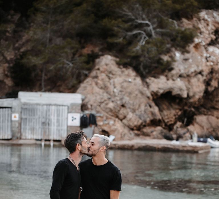 Grooms walk along the beach together as they kiss