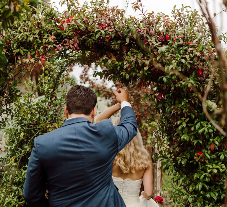 The bride leading the groom through an archway of flowers at their Italy elopement