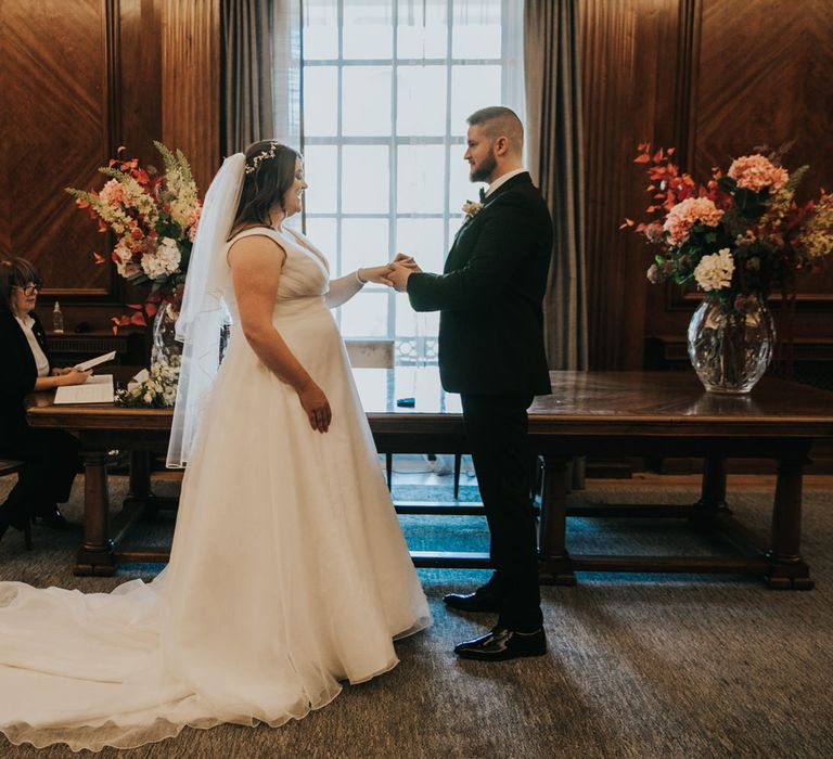 Bride & groom hold hands during wedding ceremony as light shines through the window behind them