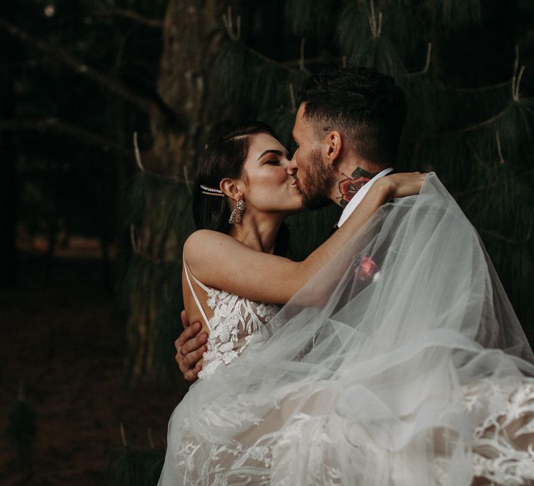 Bride and groom kissing as he carries her through the woods