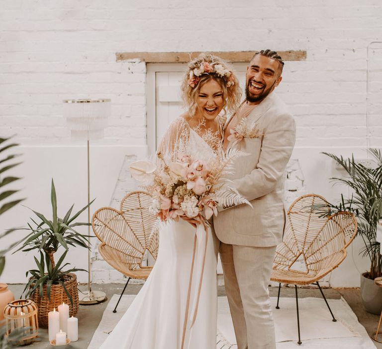 Bride and groom at tropical wedding altar with pink and white florals and a cream suit