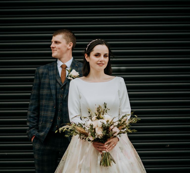 Bride and groom portrait with the bride standing in the foreground holding a peony wedding bouquet 