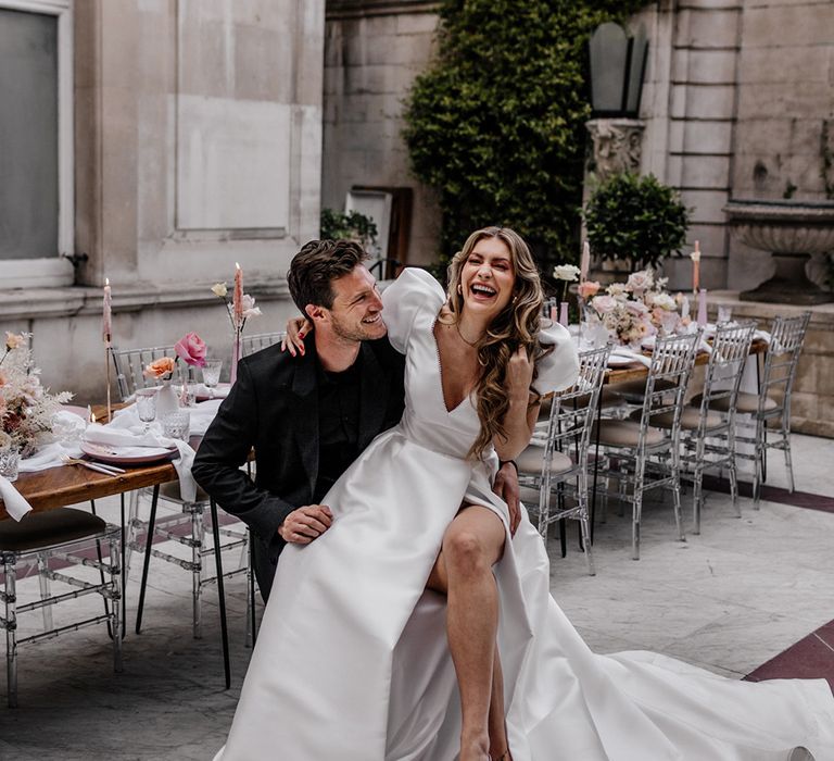 Bride in a front split Love In Lace Bridal gown and pink mules sitting on her husbands lap at their luxury wedding 