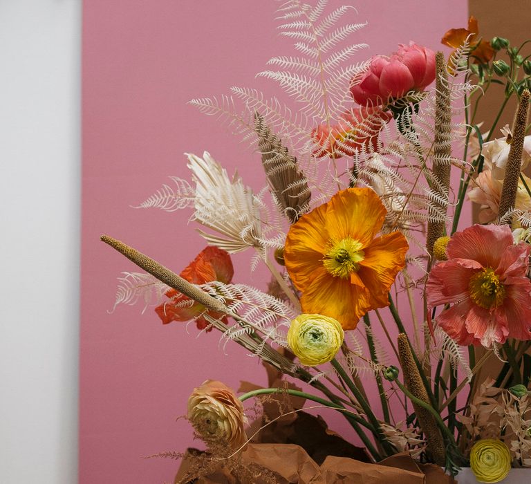 Pink, orange and dried flower bouquet in front of a dusty pink background