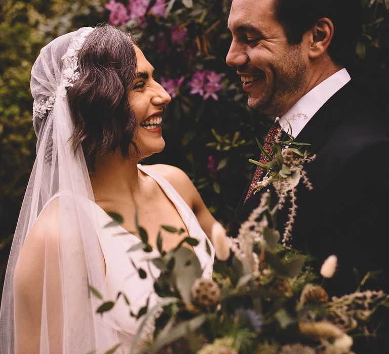 Bride with short wavy hair wearing a lace cap Juliet wedding veil smiling at her groom 