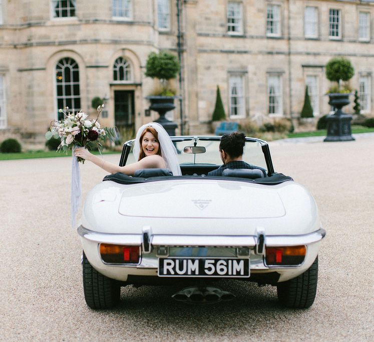 Bride and groom riding in a white convertible in front of Grantley Hall wedding venue 