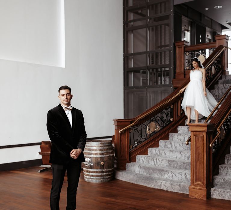 Groom waits for bride at the end of staircase for first look moment on their wedding day