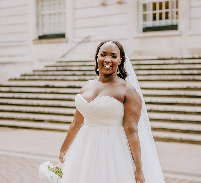 Bride wears sweetheart neckline bridal gown with full skirt and hair slicked back into natural curls and floor-length veil