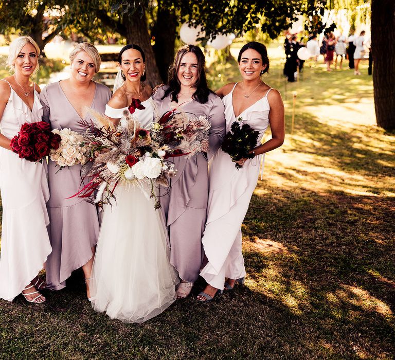 Bridesmaids in pastel dresses and blush and red rose bouquets