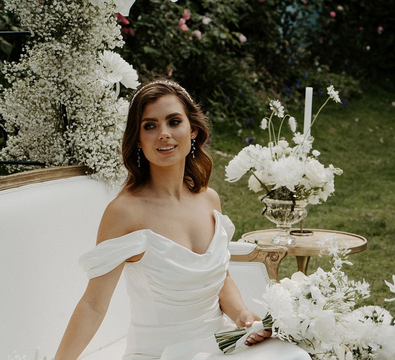 Bride with shoulder length brunette hair in an off the shoulder duchess satin wedding dress with ruched bodice at an outdoor tea party 