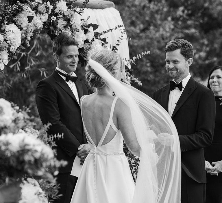 Black and white portrait of the bride and groom exchanging vows at their outdoor wedding with the bride in a low back wedding dress