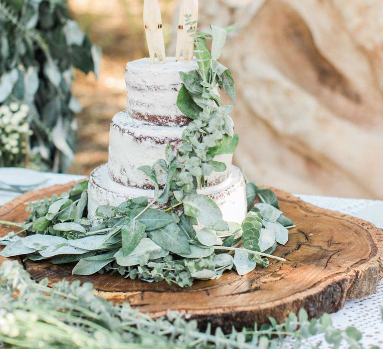 Semi naked wedding cake with foliage decor and meerkat wedding cake toppers 