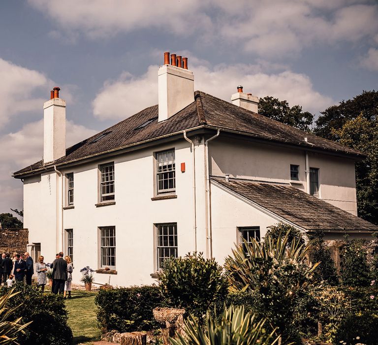 Exterior of white house in Cornwall with wedding guests in garden for wedding