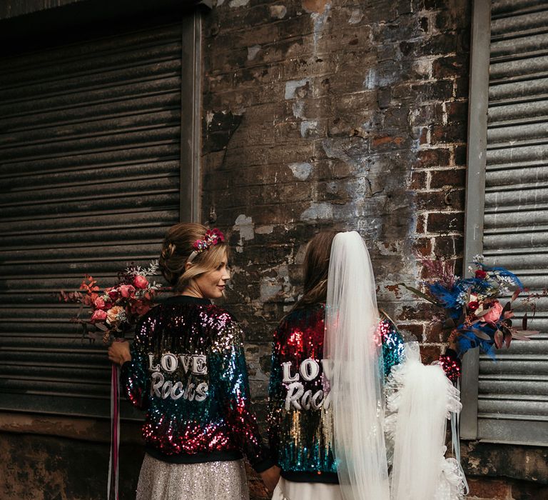 Two brides in multi coloured sequin wedding jackets with Love Rocks logo on the bride 