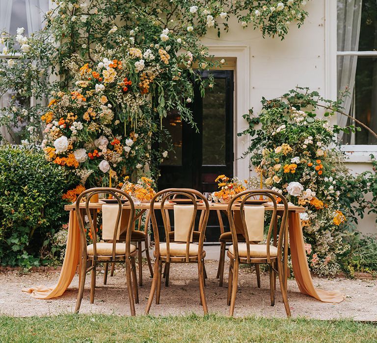 Outdoor wedding reception at Modern Hall, London with wooden chairs, orange flowers and table decor 