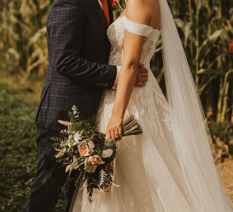 Groom kisses his bride in off the shoulder wedding dress clutching bouquet 