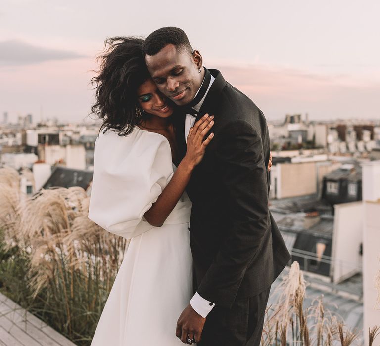 Groom in a tuxedo embracing his bride in a puff sleeve wedding dress with green eyeshadow 