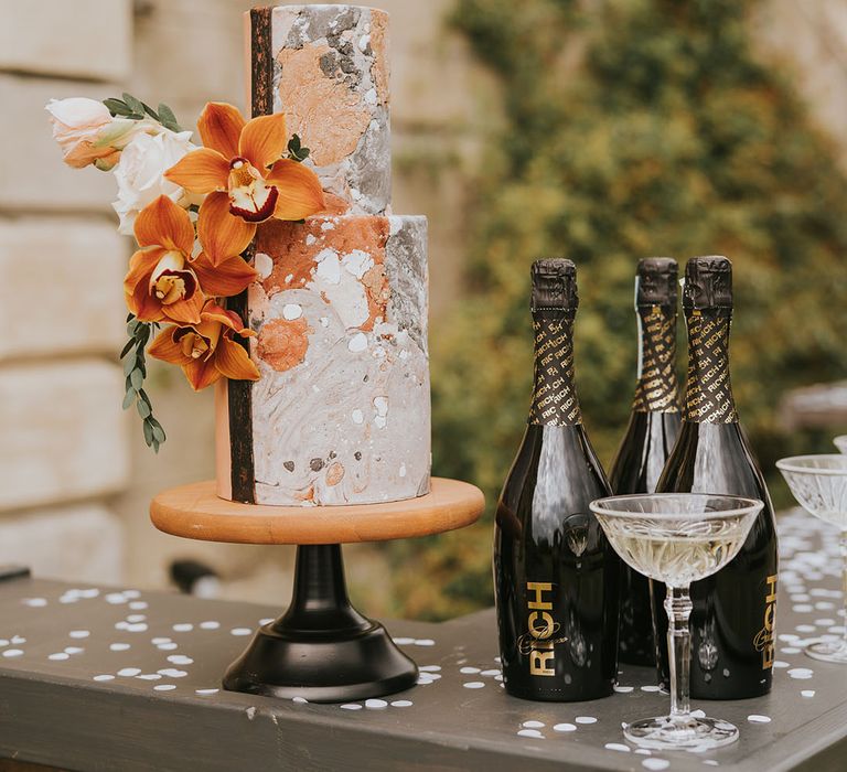 Grey, orange and white marble wedding cake by Avant Garde Cake Studio on a wood and black cake stand decorated with tropical flowers 