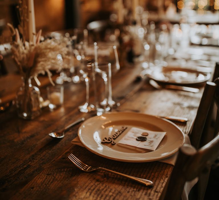 Rustic wedding table setting with dried florals, wooden table and fairy lights for barn wedding reception