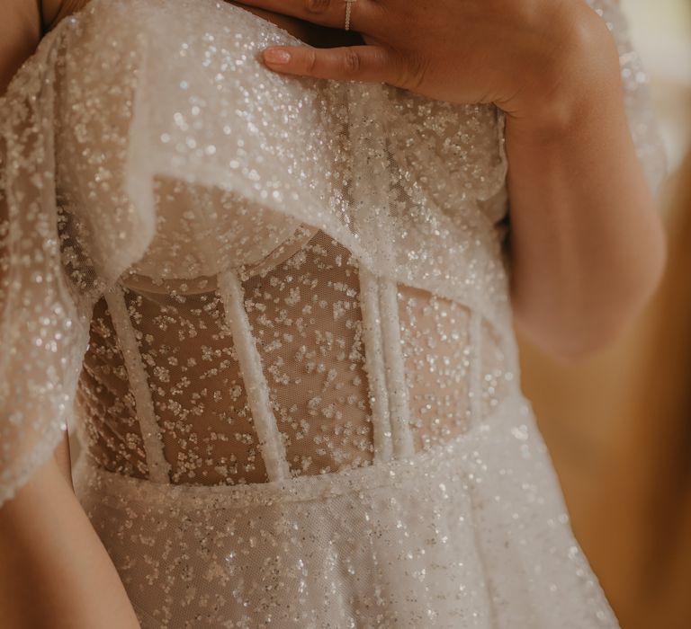 Bride in strapless sheer sparkly wedding dress with golden pearl drop necklace and glittery nail polish