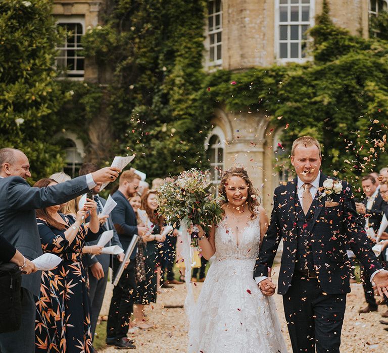 Wedding guests throw confetti over the bride and groom after their outdoor ceremony at country house 