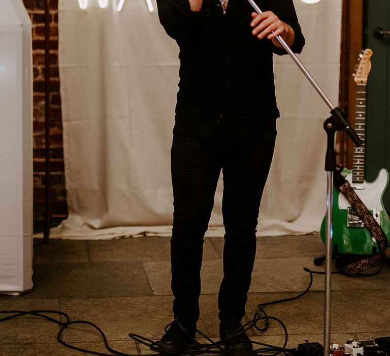 Live singer entertainment fro wedding standing in front of white neon sign personalised with the couples' last name