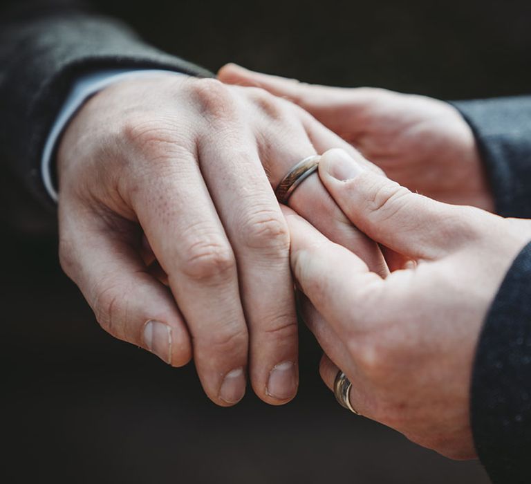 Groom puts on groom's wedding band with wood inlaid