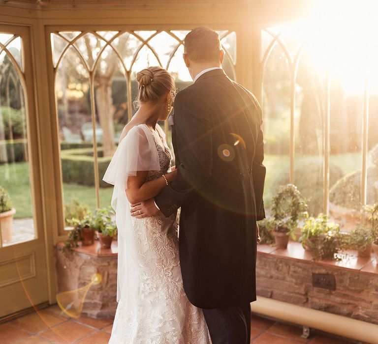 Bride and groom hug each other as they look out at the gardens around Dewsall Court 